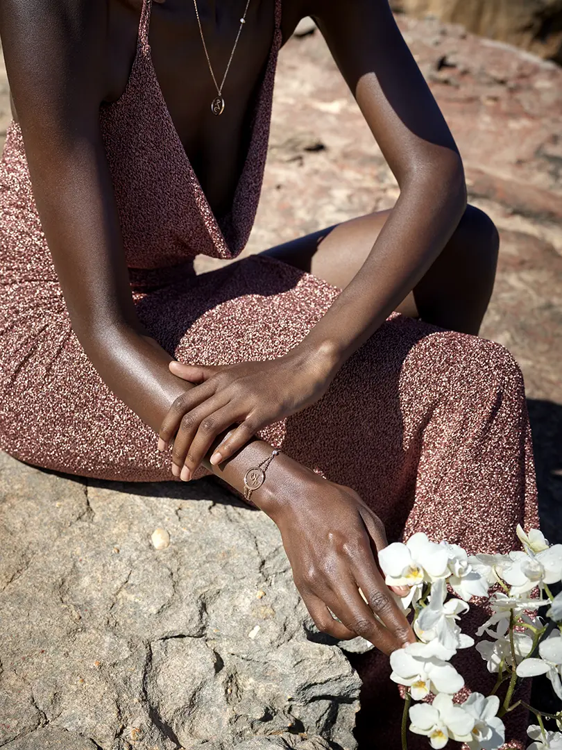Contraste saisissant : notre mannequin, entouré du désert d'Afrique, prend soin d'une orchidée tout en portant les bijoux éblouissants de Cosmos Circle, immortalisés par le talentueux photographe Ian Abela.